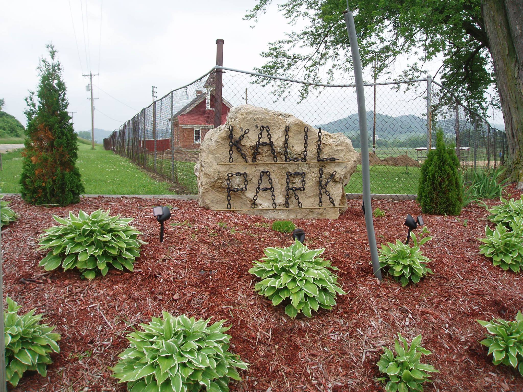 Landscaped entrance at Kaul Park featuring a large stone sign with metal lettering surrounded by mulch and green hosta plants.